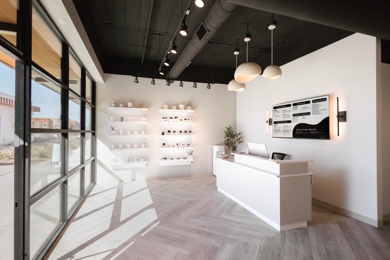 After — finished Face Foundrié interior at the Gilbert, Arizona location with reception desk, pendant lighting, product shelves, and herringbone floor