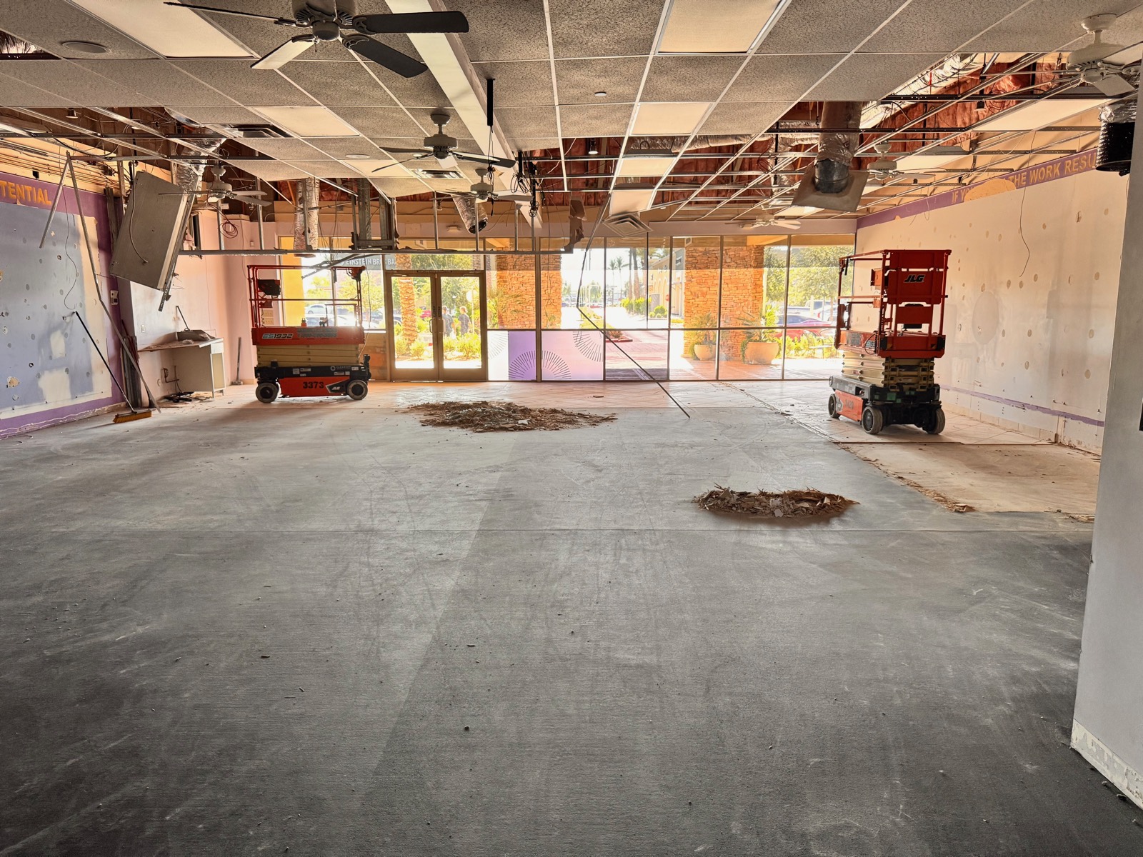 Before — gutted second-generation space with partial ceiling demolition, scissor lifts in place, and the previous tenant's wall graphics still visible