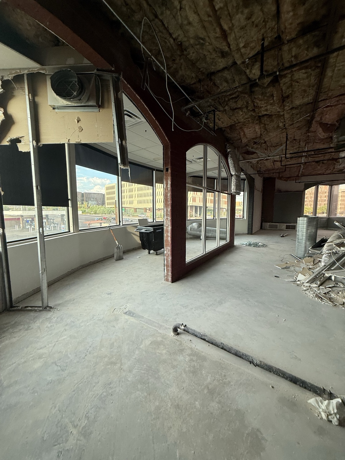 Before — mid-demolition interior at FS8 Tempe with the prior tenant's red-stained wood archway still in place, ceiling stripped to deck, and slab cut for plumbing rough-in
