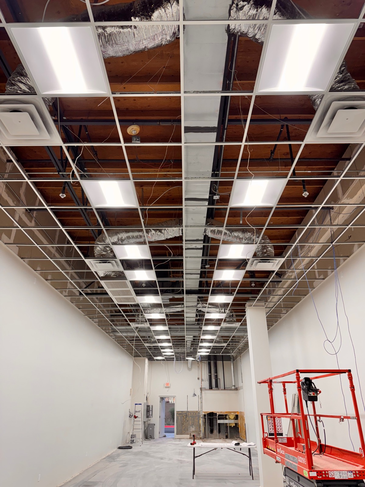 Before — ceiling grid installation underway at the future MilkShake Factory Chandler location, with newly hung light panels and exposed wood joists above