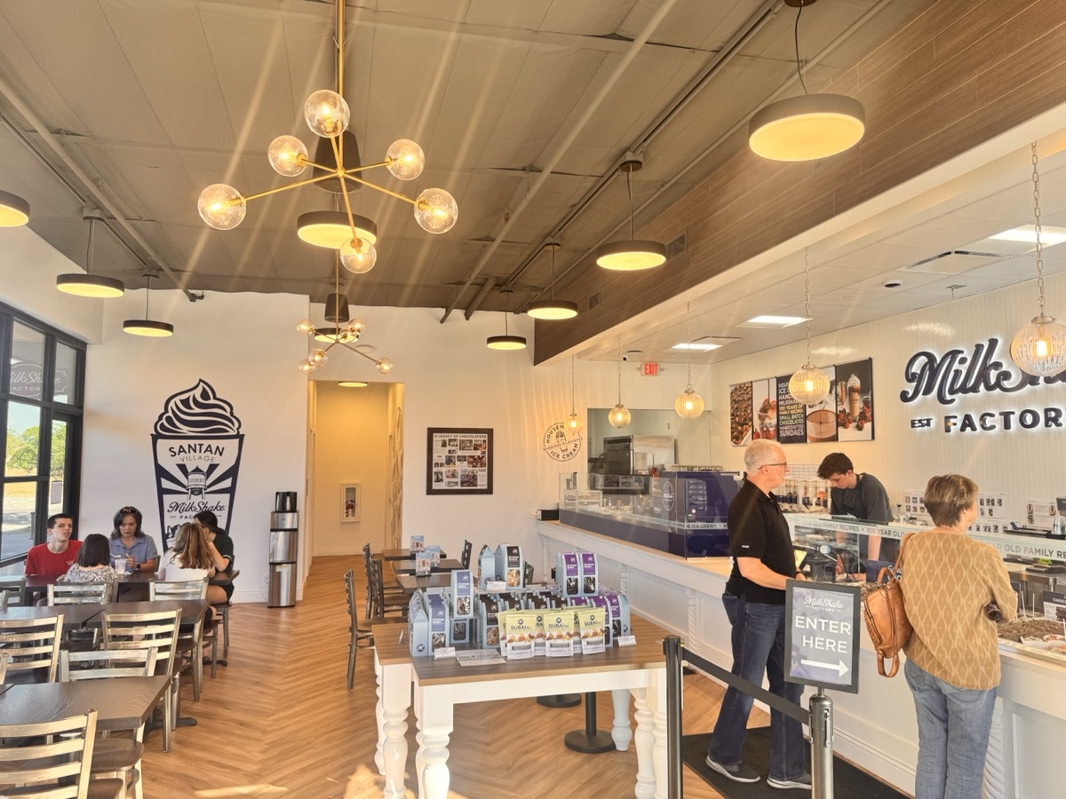 After — finished MilkShake Factory interior with brass chandeliers, Santan mural, menu boards, and customers at the service counter