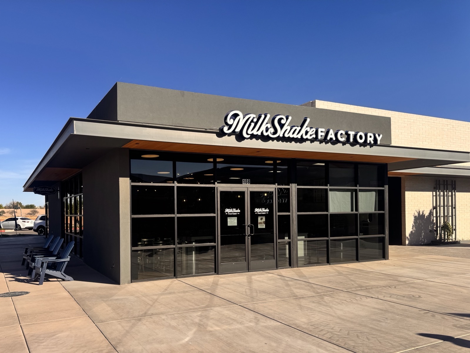 MilkShake Factory storefront exterior at the Gilbert, Arizona location — full signage visible over the entry doors under a clear blue sky, with seating and pavement foreground