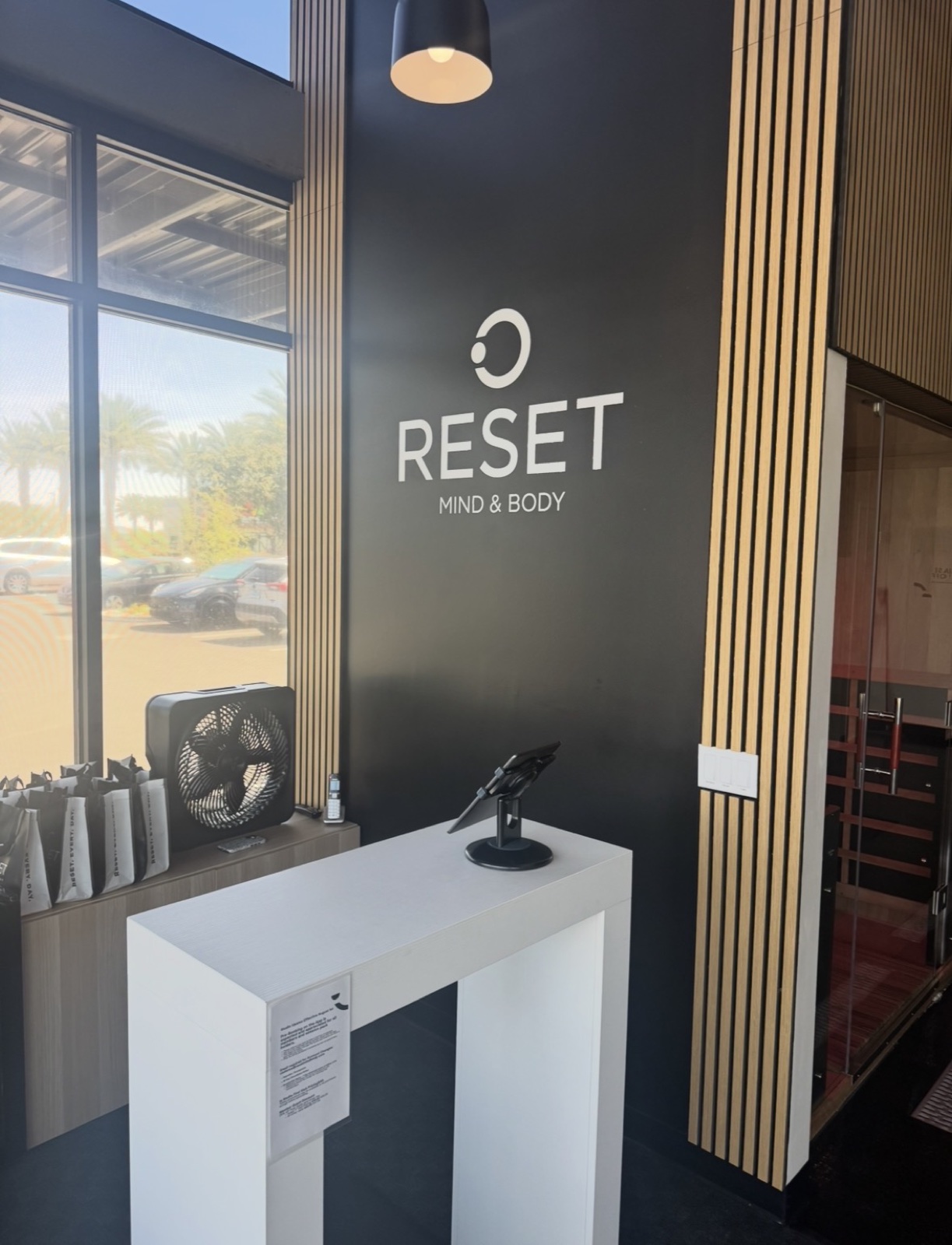 After — finished Reset Mind & Body Mesa reception area with branded logo wall, pedestal tablet stand, and slatted wood accent detailing