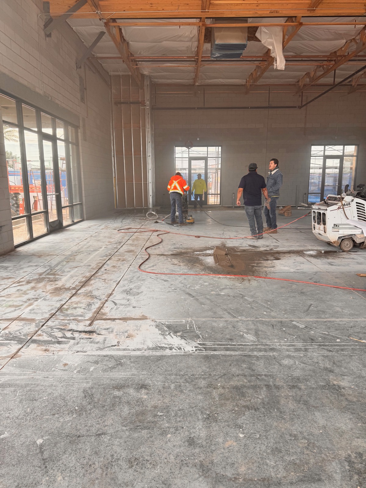Before — crew cutting the slab for plumbing rough-in at the Reset Mind Body Mesa shell space, with new storefront glazing already installed