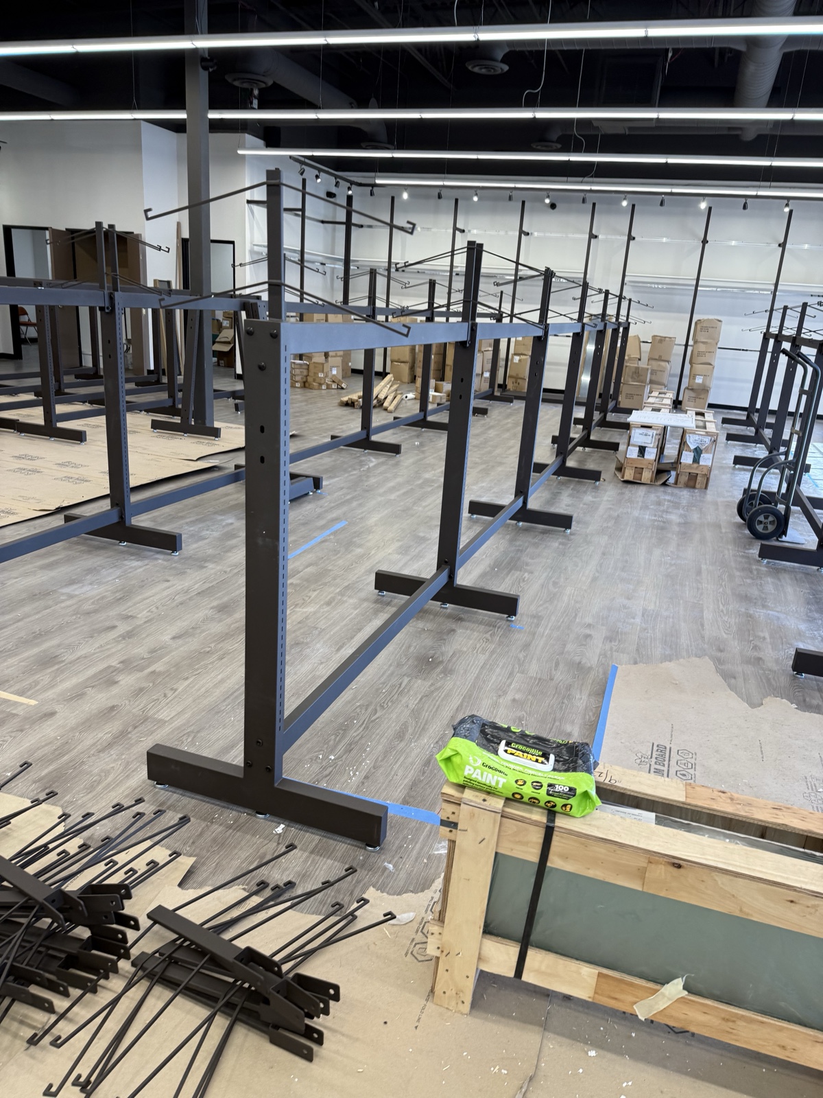 After — Uptown Cheapskate Surprise mid-build with new steel gondola fixture frames installed across the open sales floor, ceiling exposed to deck, and fixture components staged for assembly